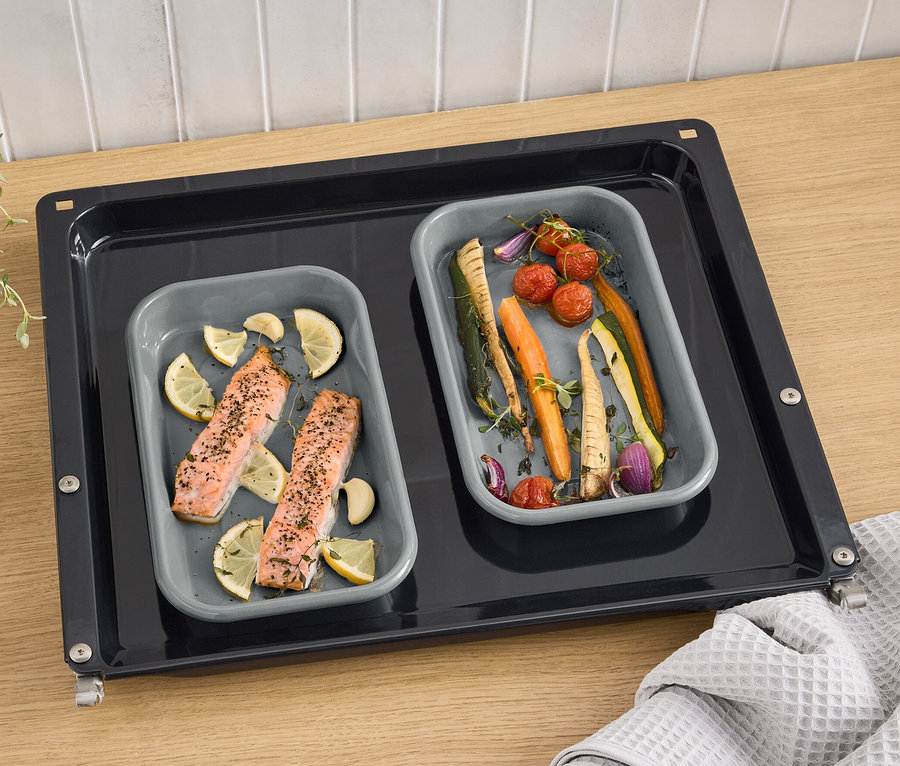 Zwei graue Emaille-Grillschalen mit Lachs, Zitrone und Gemüse auf einem Backblech.
