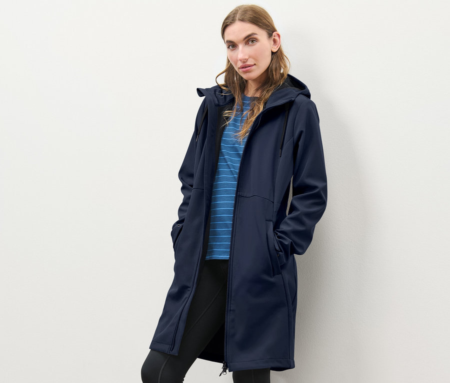 Frau posiert in einem blauen Softshellmantel.