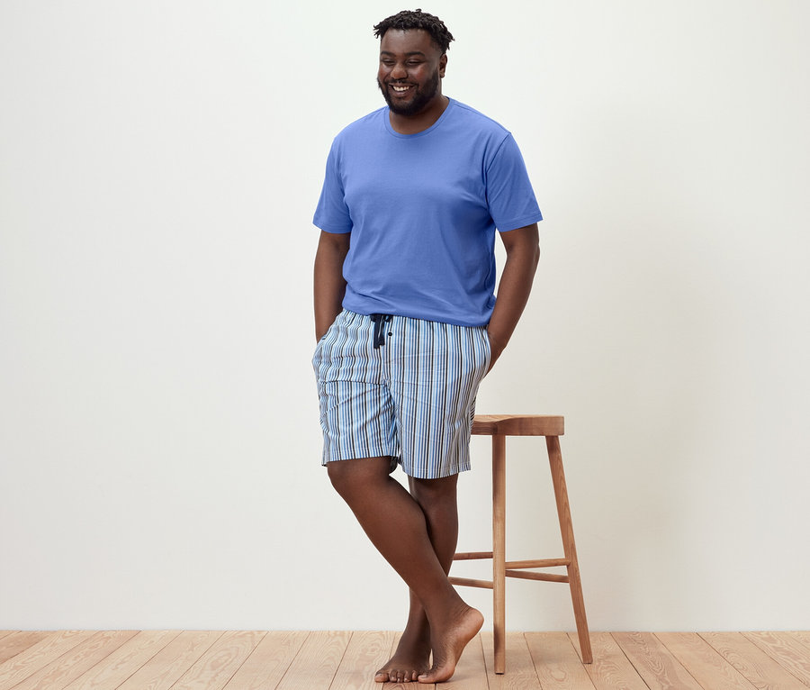 Mann lehnt an Hocker, trägt Shorty-Pyjama.