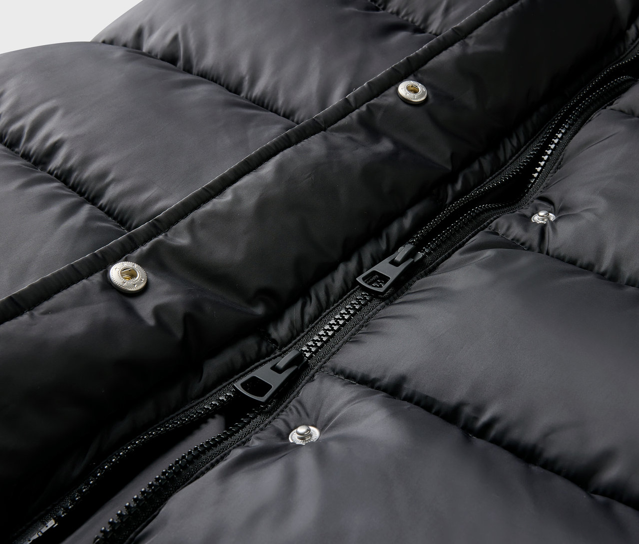 Detailaufnahme einer schwarzen Steppjacke mit Reißverschluss und Druckknöpfen.