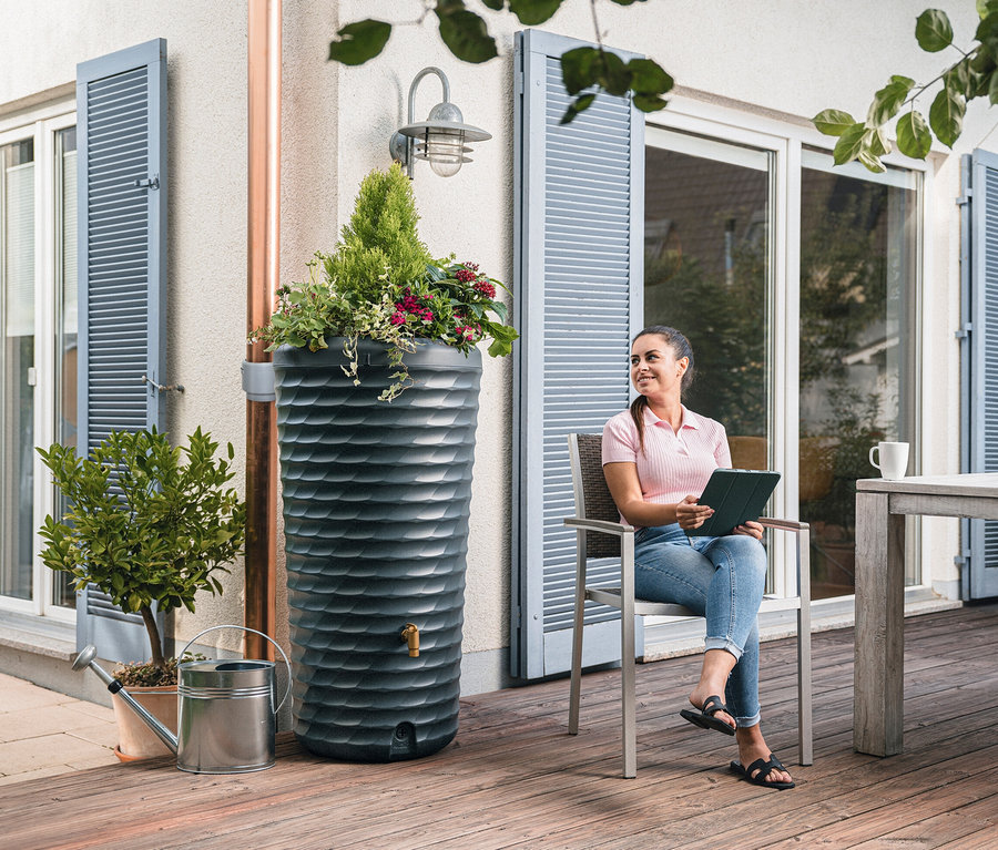 Frau sitzt neben Garantia 2-in-1-Regentonne-Komplett-Set, ca. 230 l und hält Tablet.