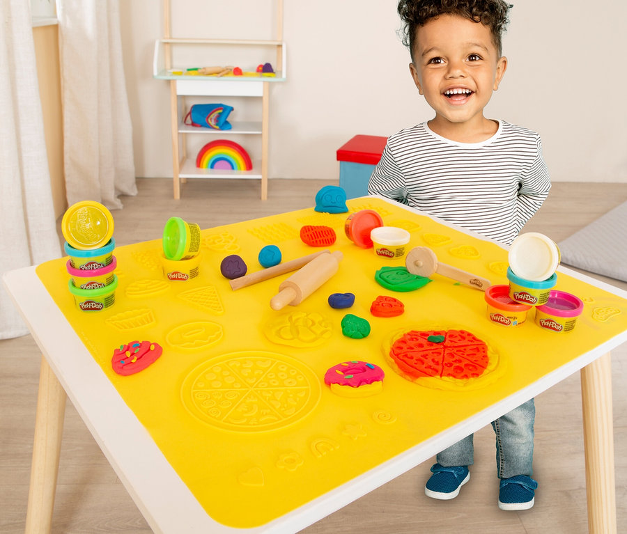 Ein Junge lacht an einem Tisch mit einem roba x Play-Doh Knet-Spielset 1.