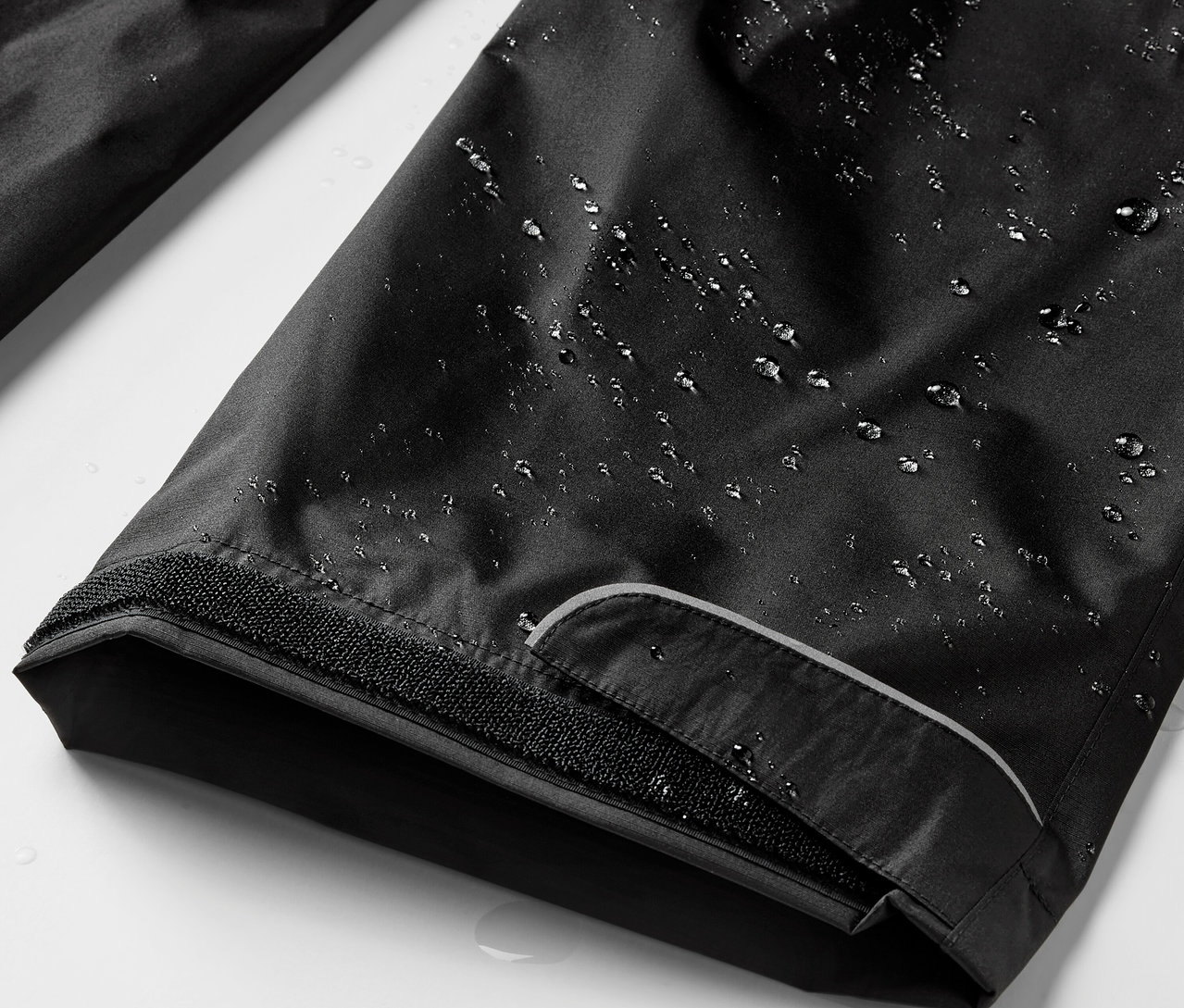 Detailaufnahme einer schwarzen Regenhose mit Wassertropfen.