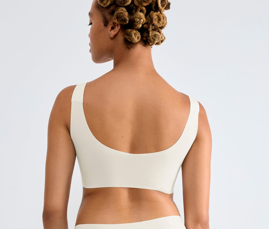 Rückansicht einer Frau mit Duttfrisur, die ein Sloggi ZERO Feel 2.0 Top in Seidenweiß und passende Unterwäsche trägt.