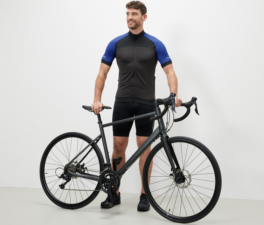 Mann steht neben einem Fahrrad und trägt ein blaues Fahrrad-Trikot.