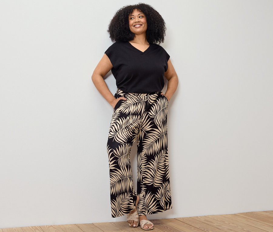 Frau posiert in schwarzem, kurzärmligem Feinstrickpullover und bedruckter Palazzohose.