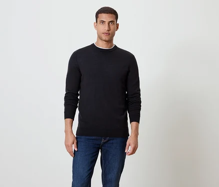 Ein Mann steht und trägt einen schwarzen Pullover und blaue Jeans.