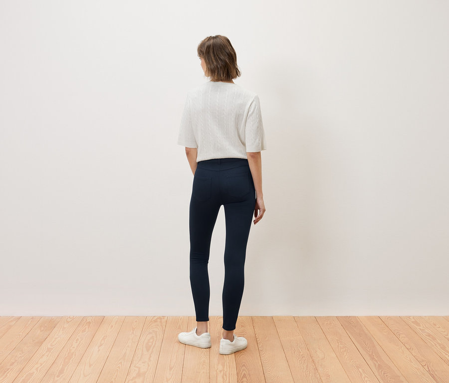 Eine Frau steht mit dem Rücken zur Kamera und trägt ein weißes Oberteil und dunkelblaue Jeans.