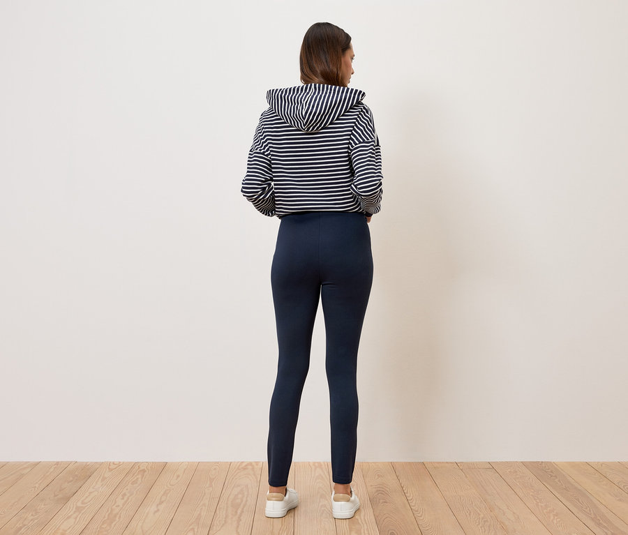 Frau steht mit dem Rücken zur Kamera und trägt einen gestreiften Kapuzenpullover und dunkelblaue Leggings.