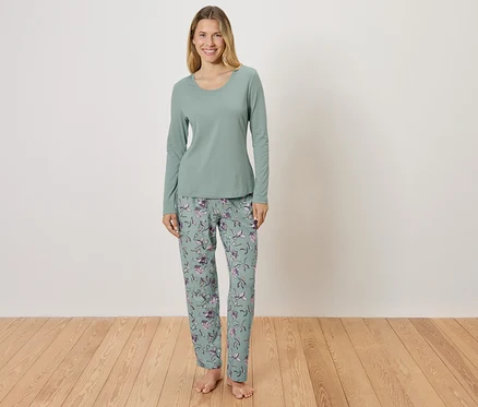 Frau steht und trägt einen grünen Pyjama mit Blumenmuster.