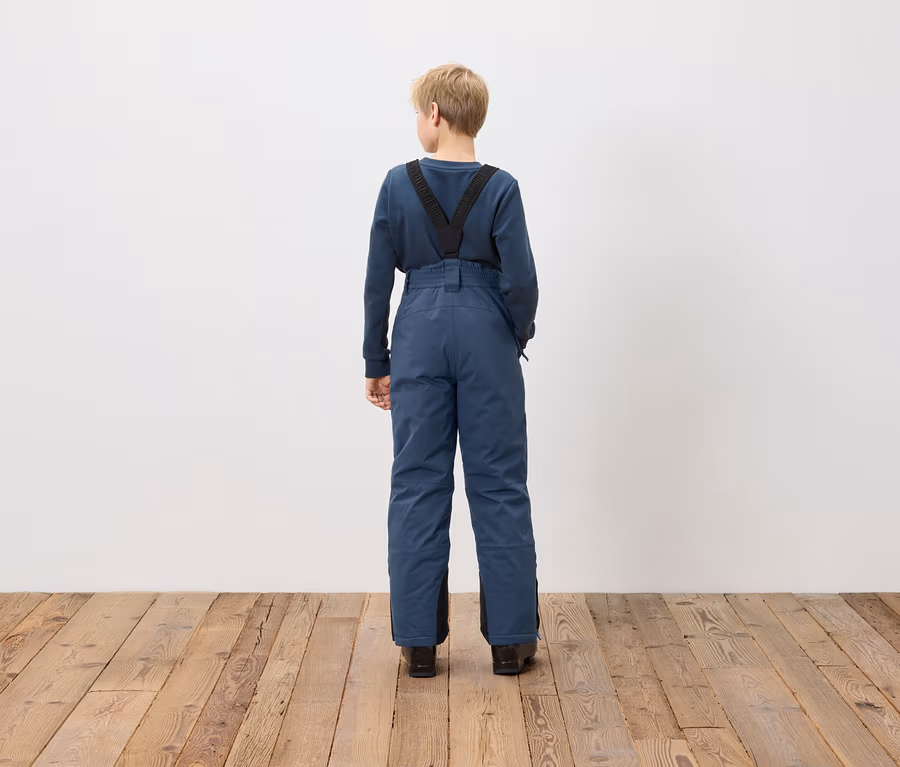 Junge steht mit dem Rücken zur Kamera und trägt blaue Latzhose.