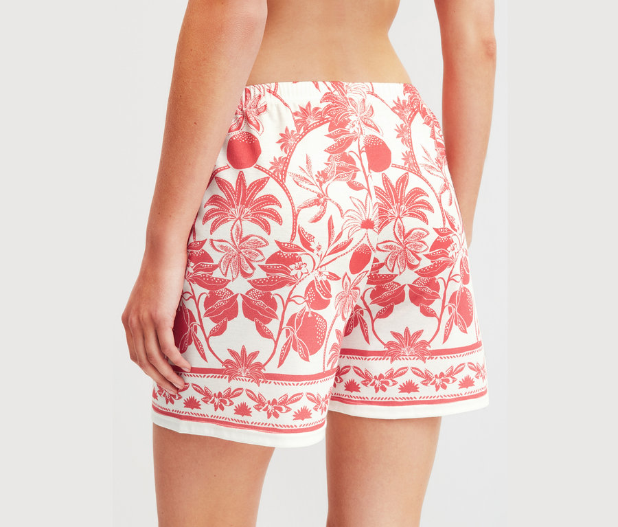 Nahaufnahme einer Frau von hinten, die kurze, locker sitzende Shorts mit einem roten Blumen- und Fruchtmuster trägt.