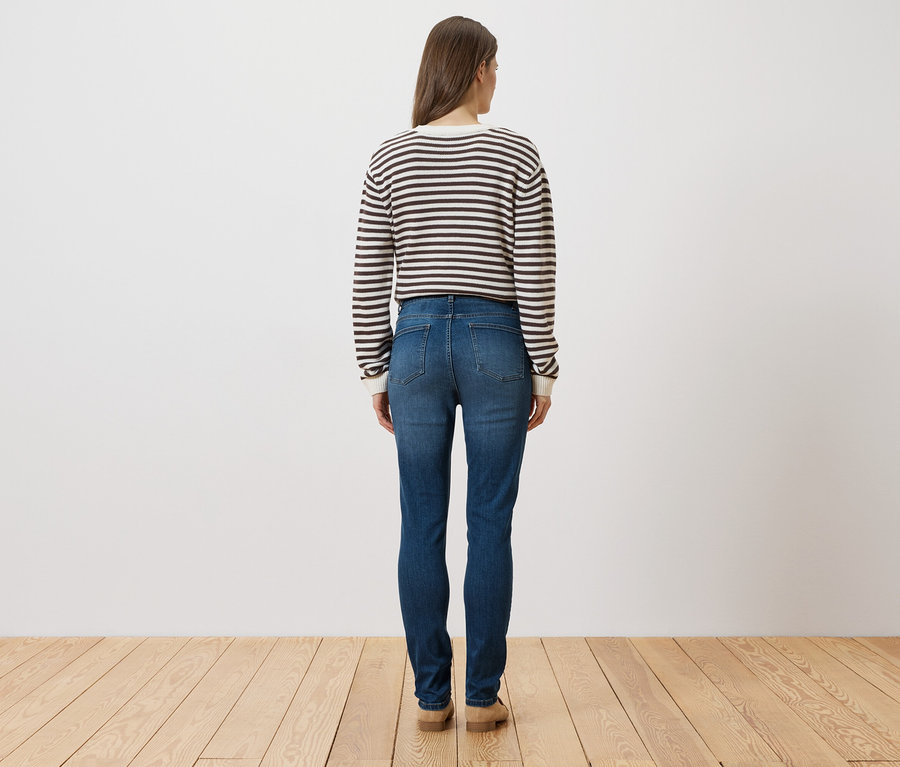 Eine Frau steht mit dem Rücken zur Kamera und trägt einen gestreiften Pullover, Jeans und Schuhe.
