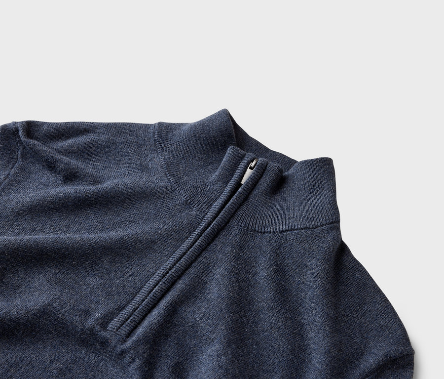 Detailansicht eines marineblauen Pullovers mit kurzem Reißverschluss am Kragen.