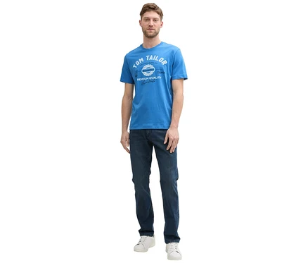 Mann in Jeans und weißen Sneakern trägt ein Tom Tailor T-Shirt mit Logo in Sapphire Blue.