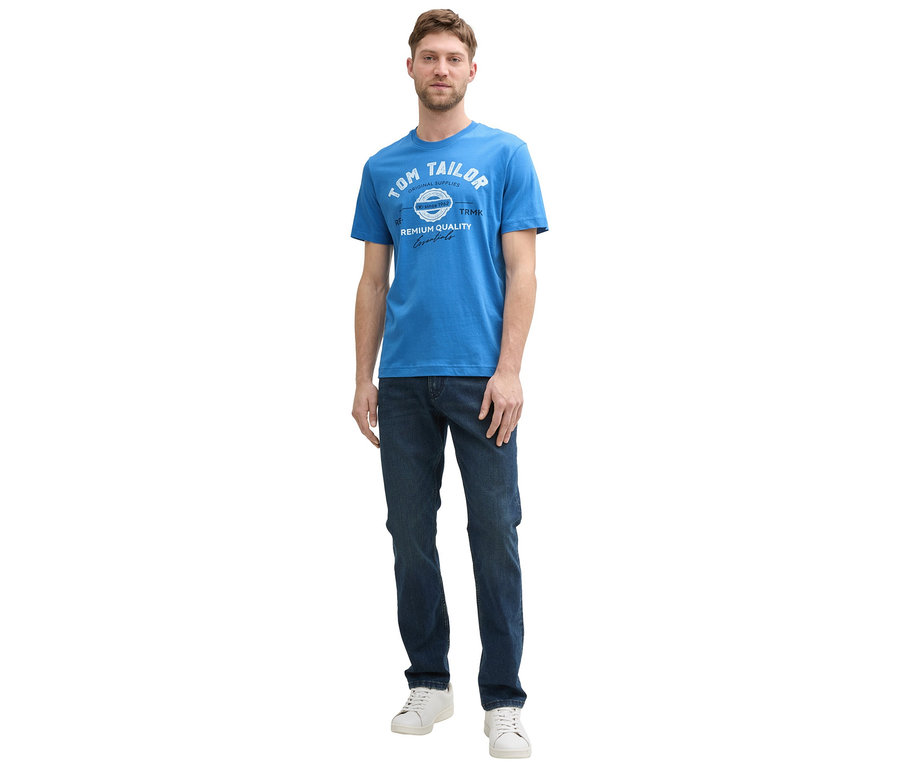 Mann in Jeans und weißen Sneakern trägt ein Tom Tailor T-Shirt mit Logo in Sapphire Blue.