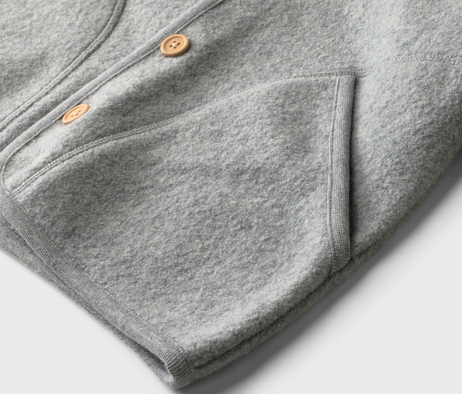 Detailansicht einer hellgrauen Jacke mit zwei Knöpfen und einer aufgesetzten Tasche.