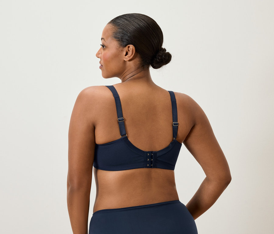 Rückansicht einer Frau mit Dutt, die einen marineblauen BH und Unterwäsche trägt.