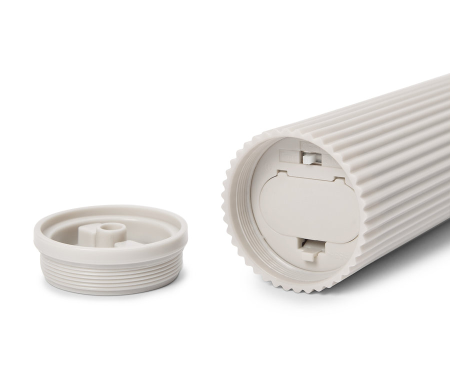 Ein cremefarbener, geriffelter, zylindrischer Behälter liegt auf der Seite, wobei der Deckel daneben liegt.