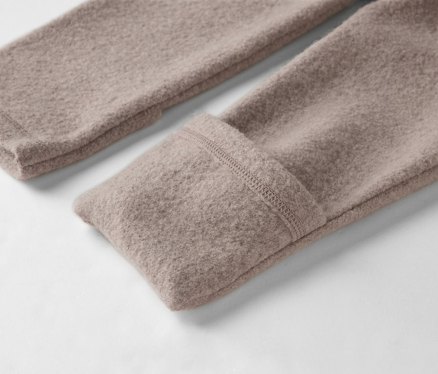 Nahaufnahme von zwei Ärmeln eines hellbraunen Wollpullovers auf weißem Hintergrund.