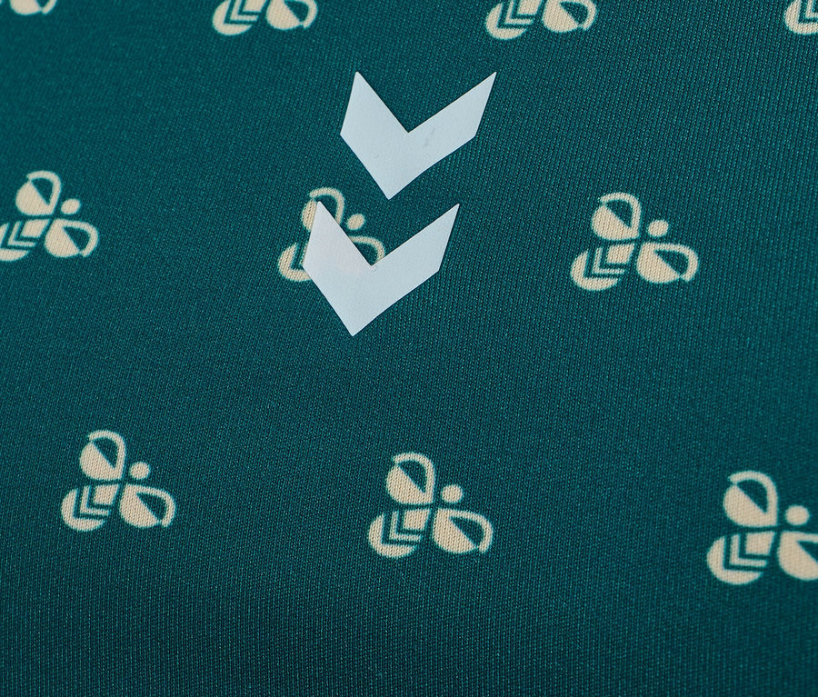 Nahaufnahme eines grünen Stoffes mit einem Muster aus cremefarbenen Hummel-Logos und weißen Chevrons.