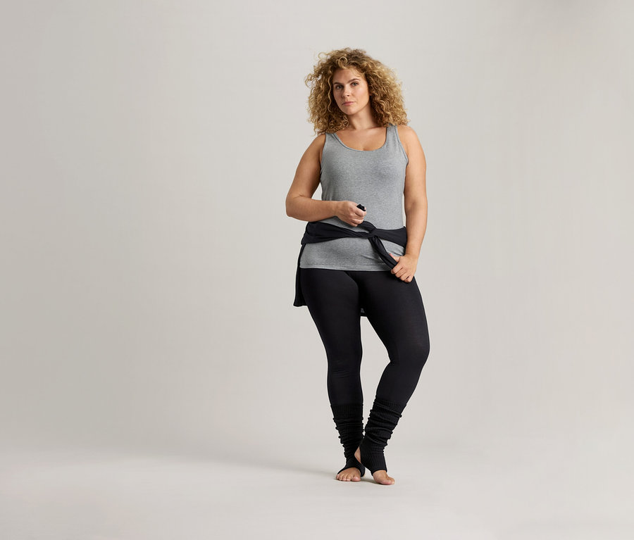 Frau mit lockigem Haar trägt ein graues Tanktop und schwarze Leggings.