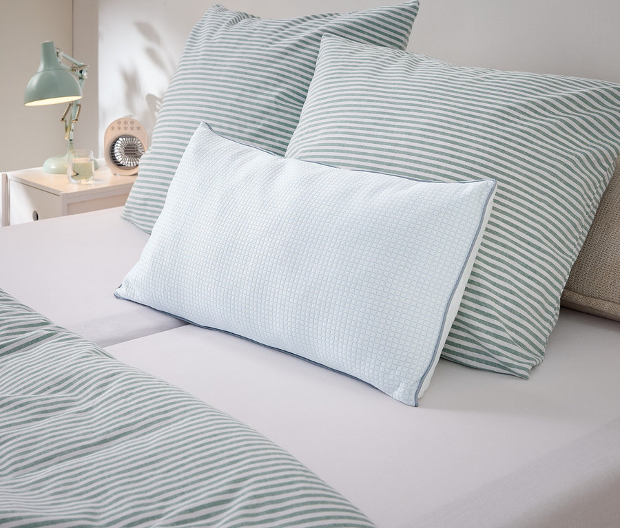 Nahaufnahme von Kissen und Bettwäsche mit Streifenmuster in Weiß und Grün auf einem Bett.