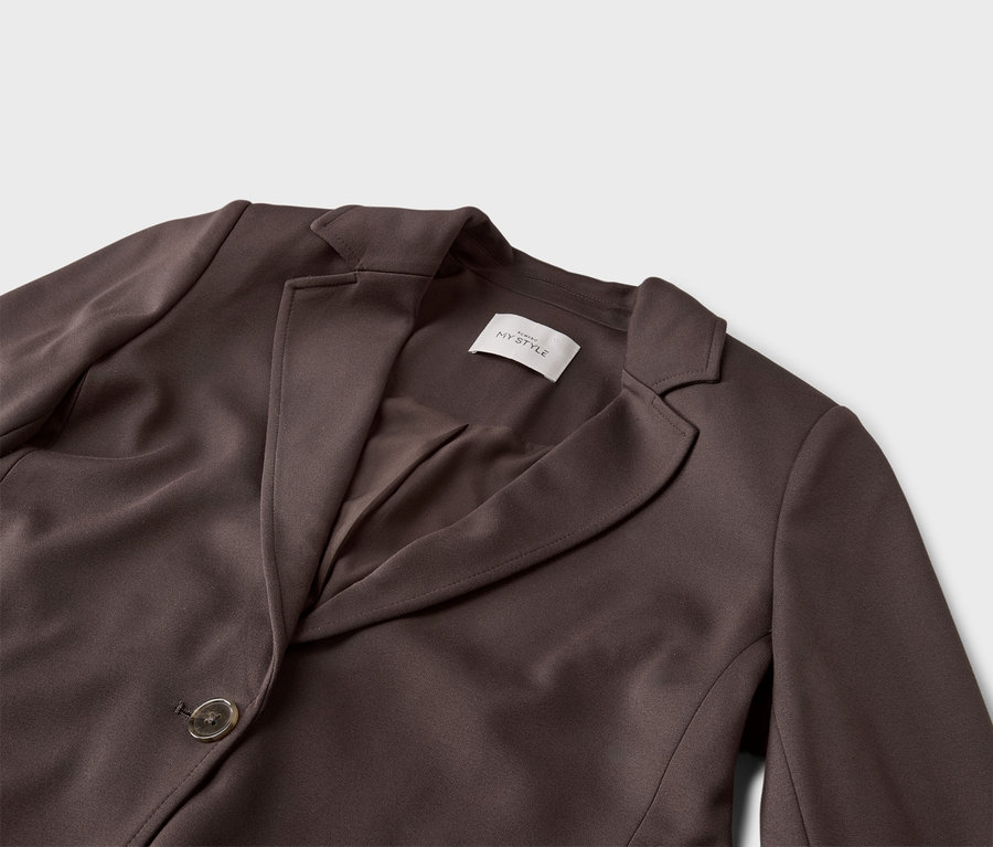 Nahaufnahme eines braunen Blazers mit Knopf und Revers auf grauem Hintergrund.