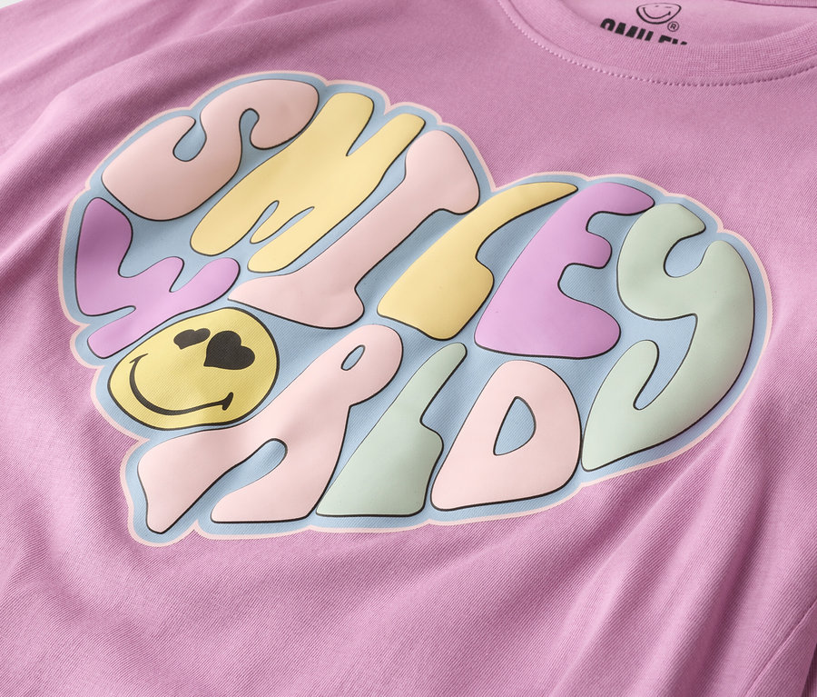 Nahaufnahme eines lila T-Shirts mit einem herzförmigen Smiley-Gesicht-Design in Pastellfarben.
