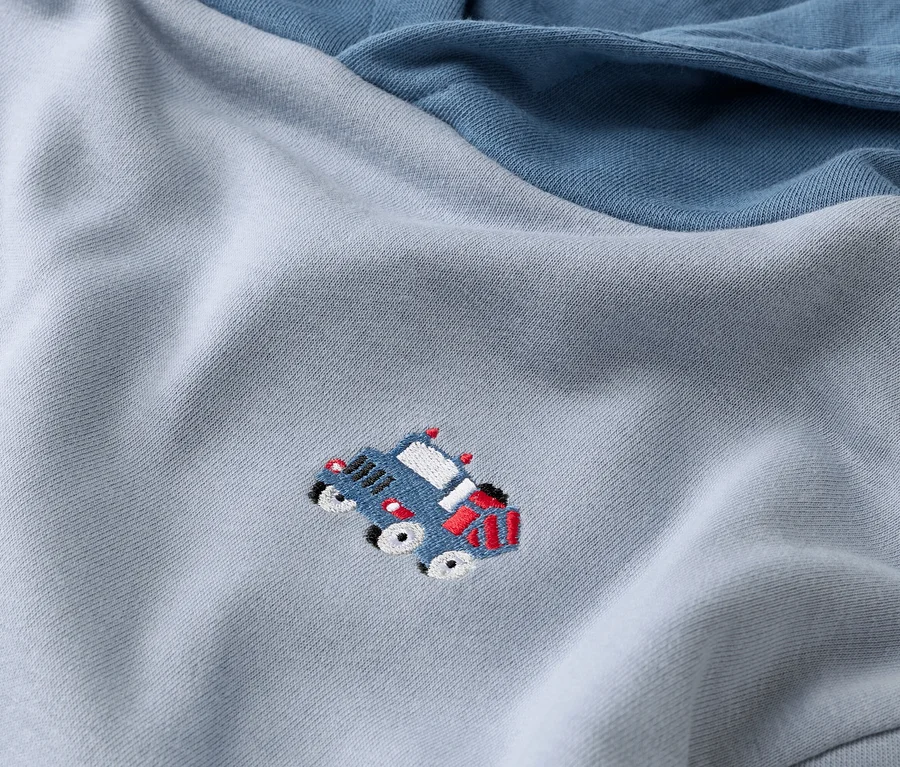 Nahaufnahme eines hellblauen Sweatshirts mit dunkelblauem Ärmel und einer blauen Autoapplikation.
