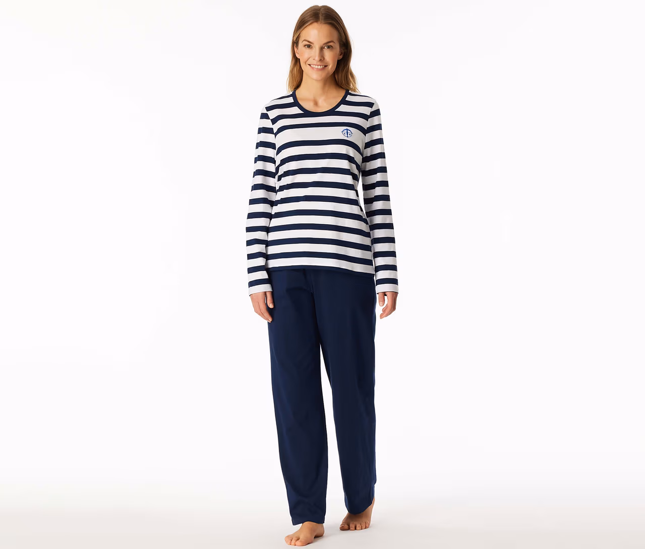 Lächelnde Frau in einem SCHIESSER Pyjama-Set: weiß-marineblau gestreiftes Langarmshirt mit Anker-Logo und marineblaue Hose, barfuß.