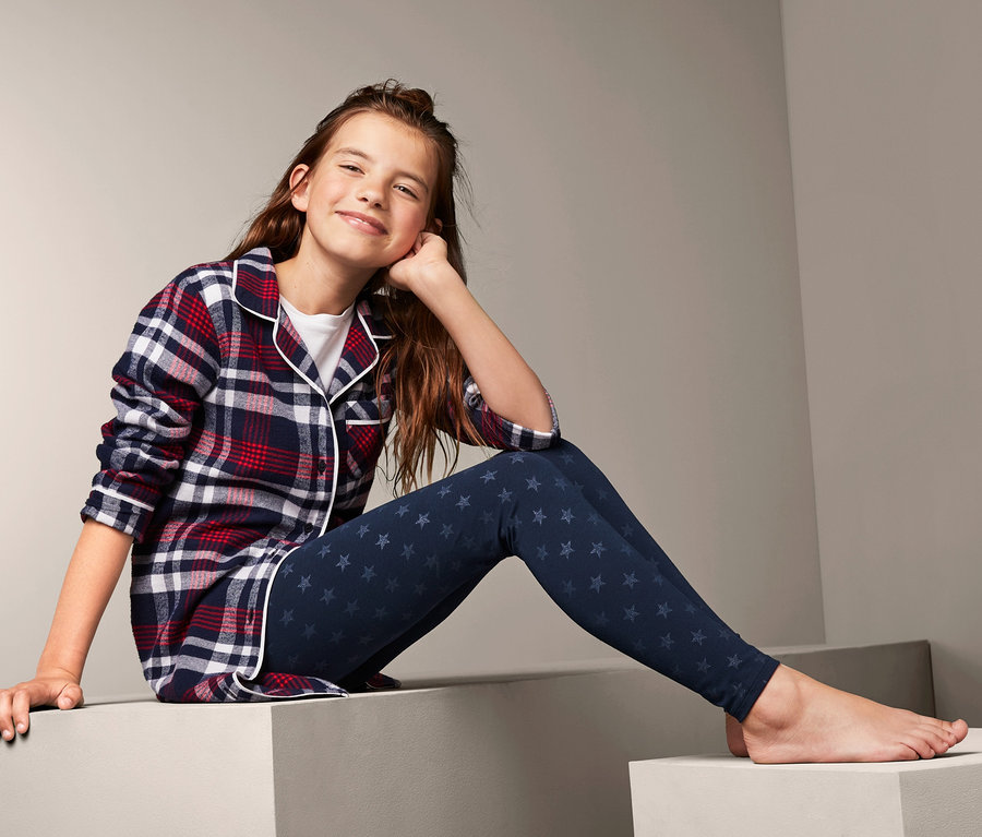 Mädchen sitzt auf Stufen und trägt ein kariertes Hemd und 2 Leggings.