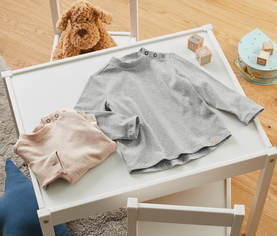 Zwei Baby-Rippshirts liegen auf einem weißen Tisch neben Bauklötzen.
