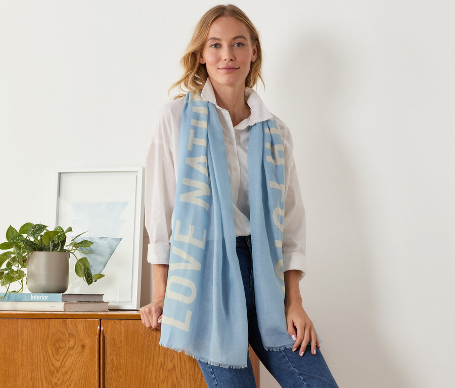 Frau lehnt an einem Schrank und trägt einen Webschal mit Statement-Print.