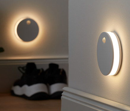 Zwei LED-Multifunktionsleuchten sind an der Wand montiert. Im Hintergrund sind eine Topfpflanze und Schuhe.