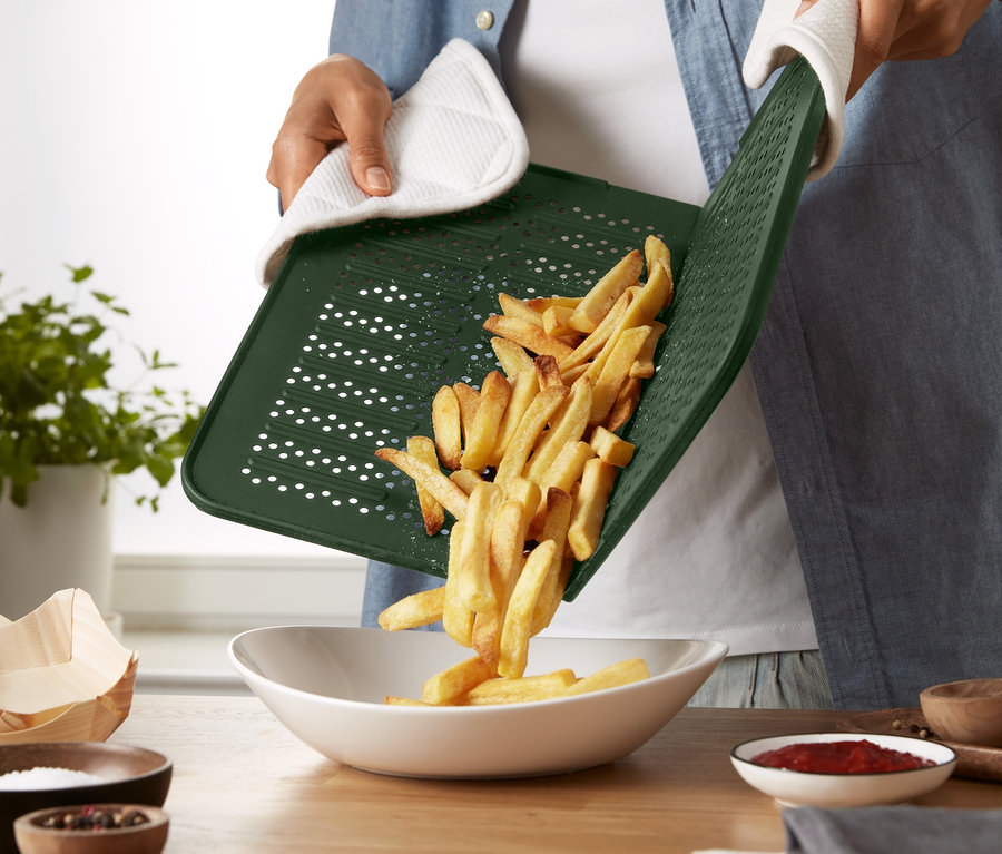 Person schüttet mit einem Ofenhandschuh Pommes von einem Silikon-Backblech in eine Schüssel.