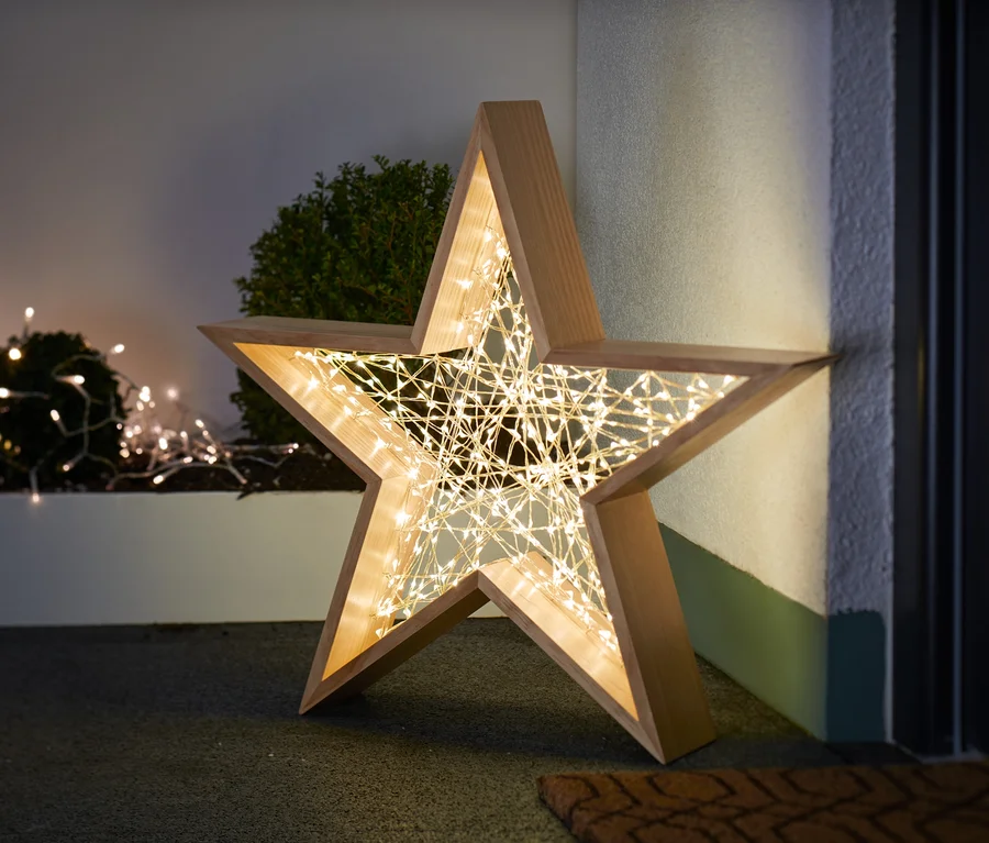 Ein LED-Outdoor-Holzstern steht auf dem Boden neben einer Wand.