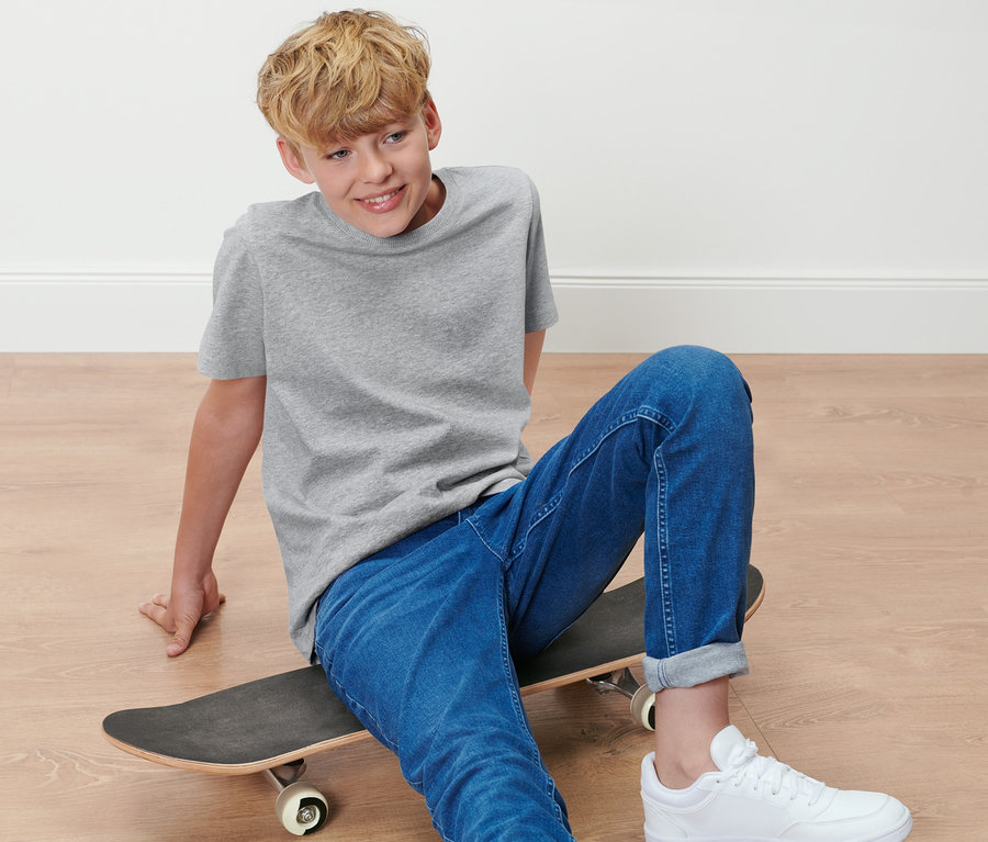 Ein Junge sitzt auf einem Skateboard und trägt ein graues T-Shirt aus einem 2er-Pack Kinder-T-Shirts.