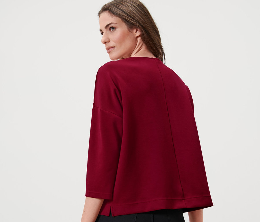 Frau trägt ein bordeauxrotes Sweatshirt mit 3/4-Arm und eine schwarze Hose.
