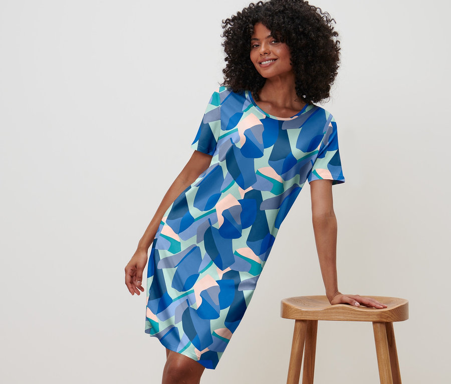 Frau posiert in blauem Nachthemd mit Muster und lehnt an einem Holzschemel.