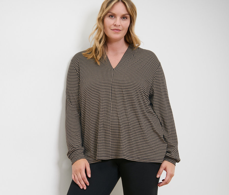 Frau posiert in bedrucktem Blusenshirt mit V-Ausschnitt und Heavy-Leggings.