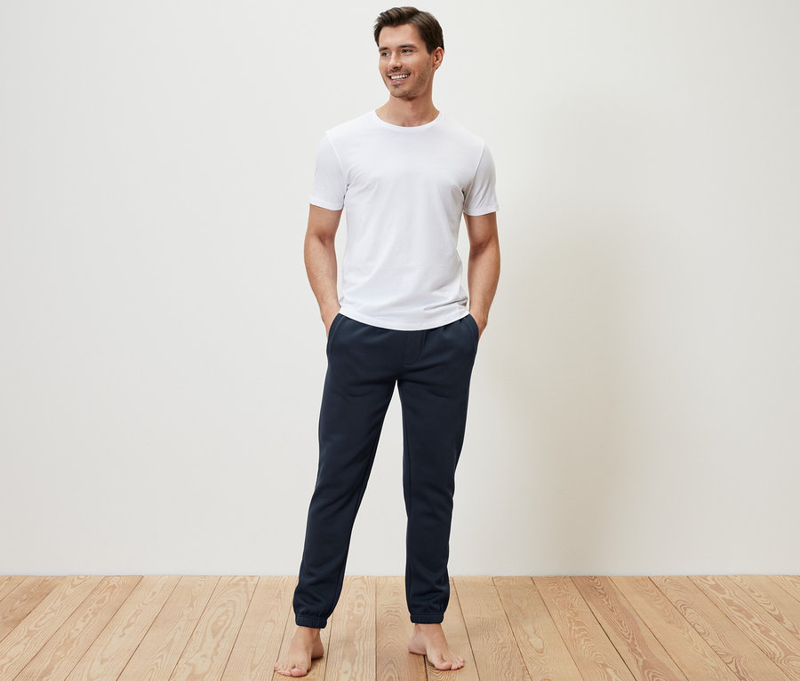 Mann steht mit Händen in den Taschen der Sweathose.