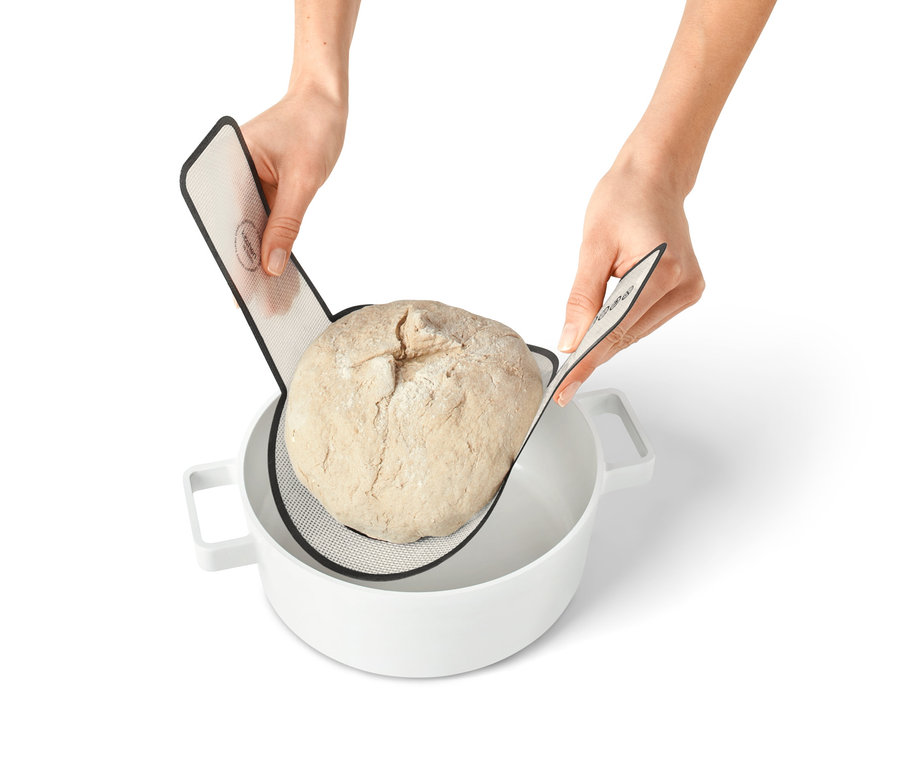 Hände legen einen Laib Brot mit einer Dauerbackmatte in eine weisse Schüssel.