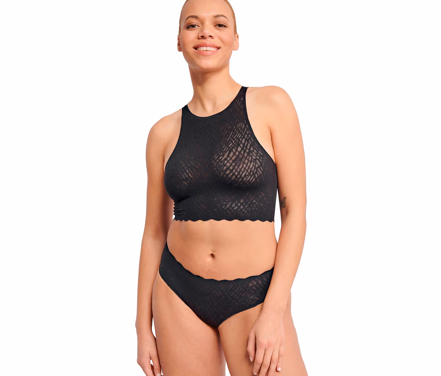 Lächelnde Frau trägt einen schwarzen hochgeschlossenen Bralette mit strukturiertem Muster und Wellenkante und schwarze sloggi ZERO Feel Bliss Hipster Unterwäsche mit Wellenkante.