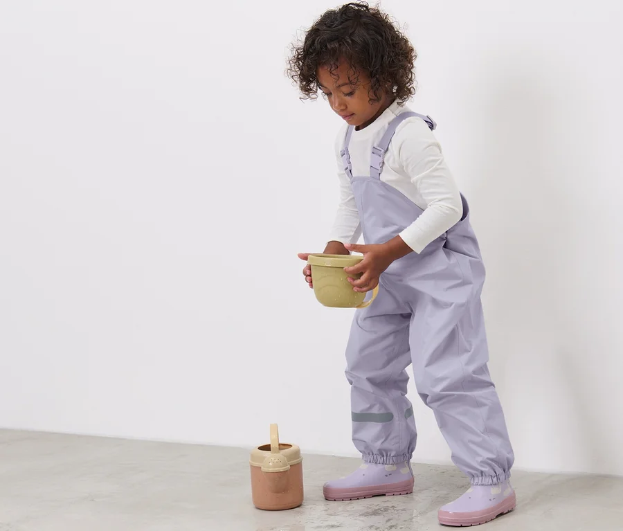 Kind hält gelben Behälter und trägt eine lila Kinder-Regenhose.