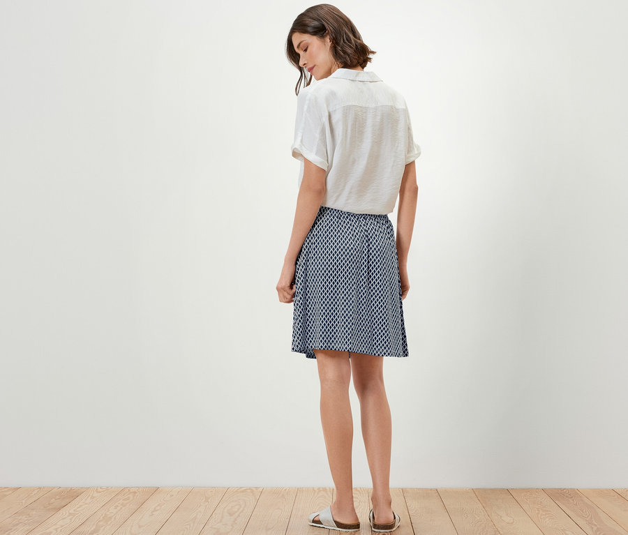 Frau steht mit dem Rücken zur Kamera und trägt ein Oberteil und einen bedruckten Jerseyrock.