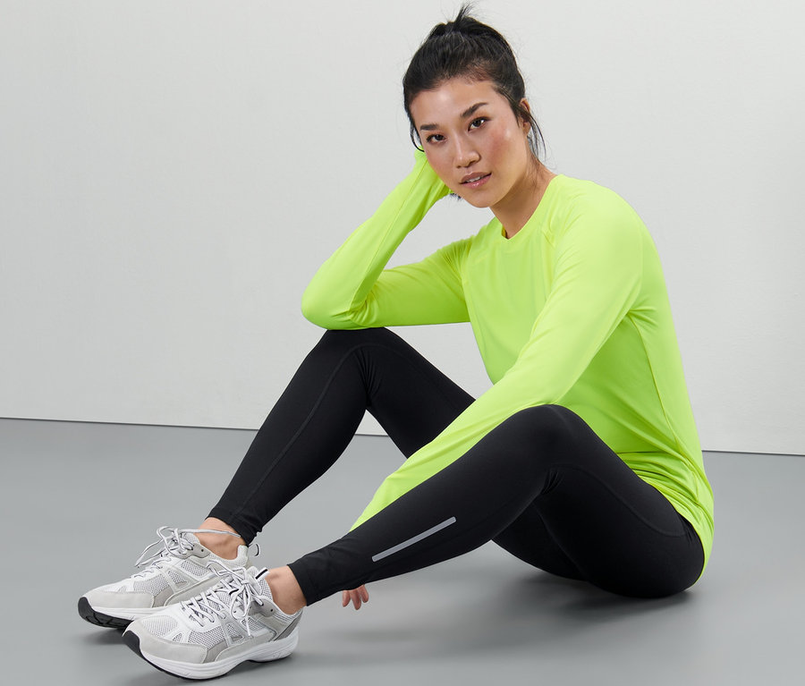 Frau sitzt am Boden und trägt eine Sporttight und ein neon-grünes Oberteil.