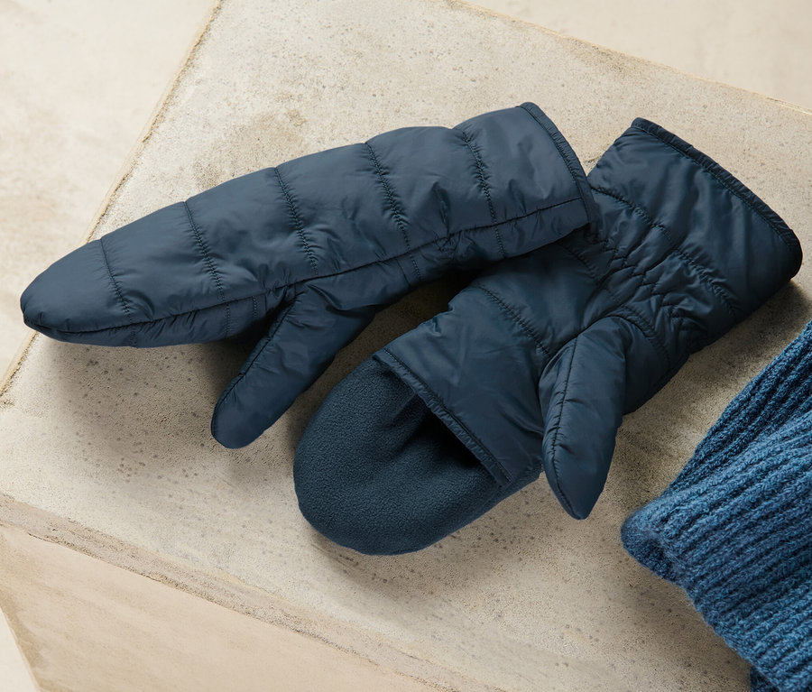 Zwei marineblaue Stepp-Klappfäustlinge liegen auf einer grauen Oberfläche neben einer blauen Strickmütze.