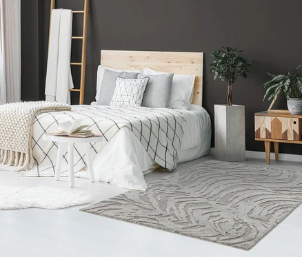 Schlafzimmer mit Bett, Holzkopfteil und grauen Kissen. Auf dem Boden liegt ein grauer Teppich »Cosmo «Waves, ca. 160 x 230 cm.