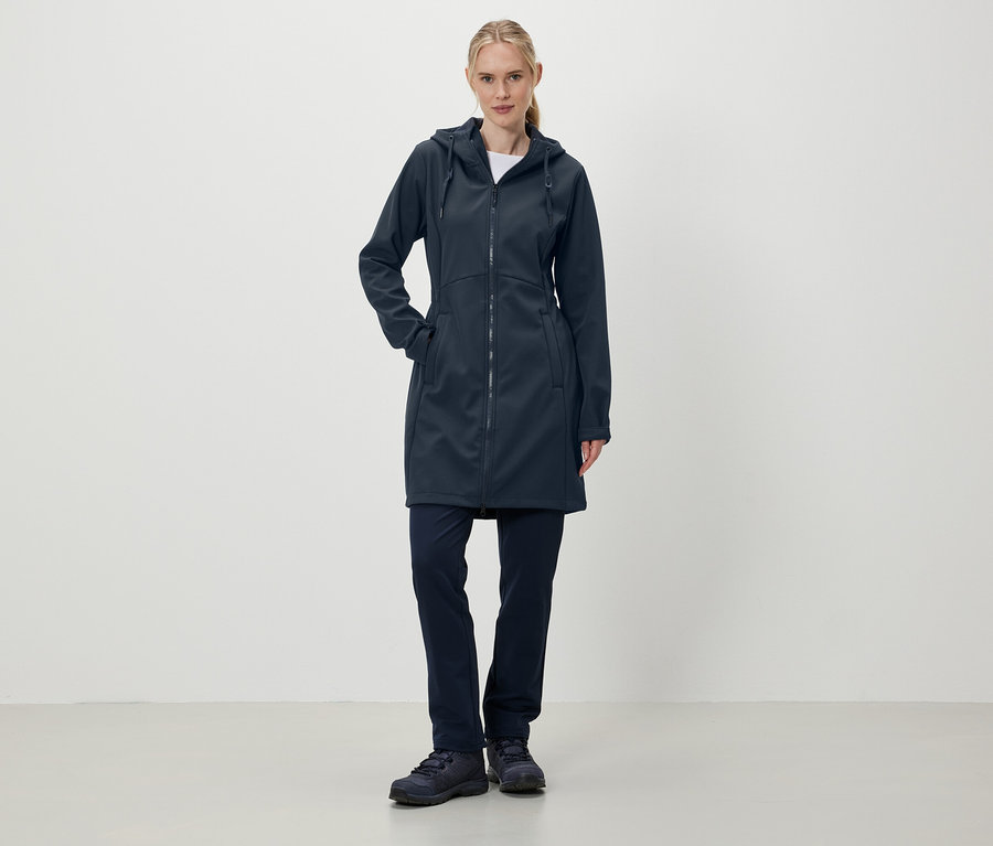 Eine Frau steht und trägt einen dunkelblauen Mantel mit Kapuze, Hose und Schuhe.